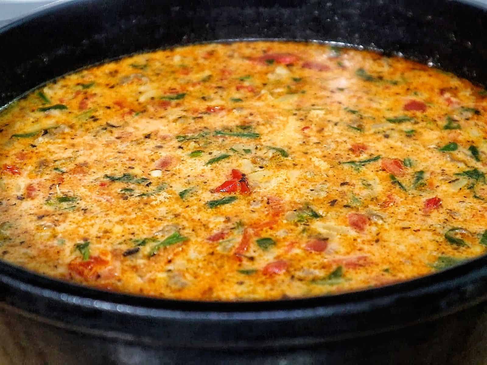 A creamy bowl of sausage orzo soup filled with tomatoes, spinach, and tender pasta, topped with fresh basil and melted Parmesan.