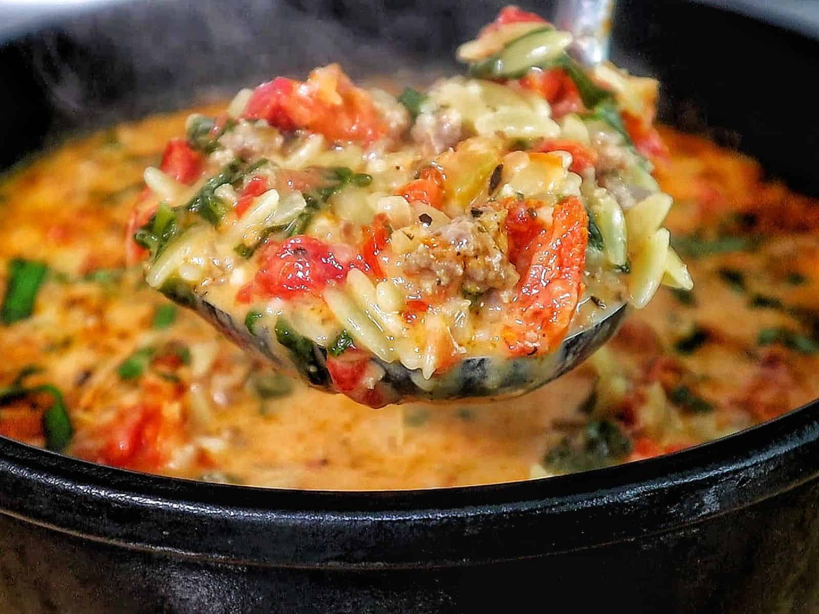 A creamy bowl of sausage orzo soup filled with tomatoes, spinach, and tender pasta, topped with fresh basil and melted Parmesan.