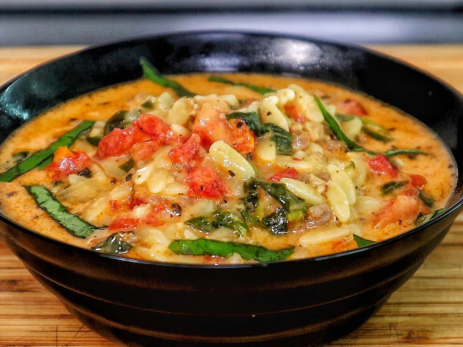A creamy bowl of sausage orzo soup filled with tomatoes, spinach, and tender pasta, topped with fresh basil and melted Parmesan.