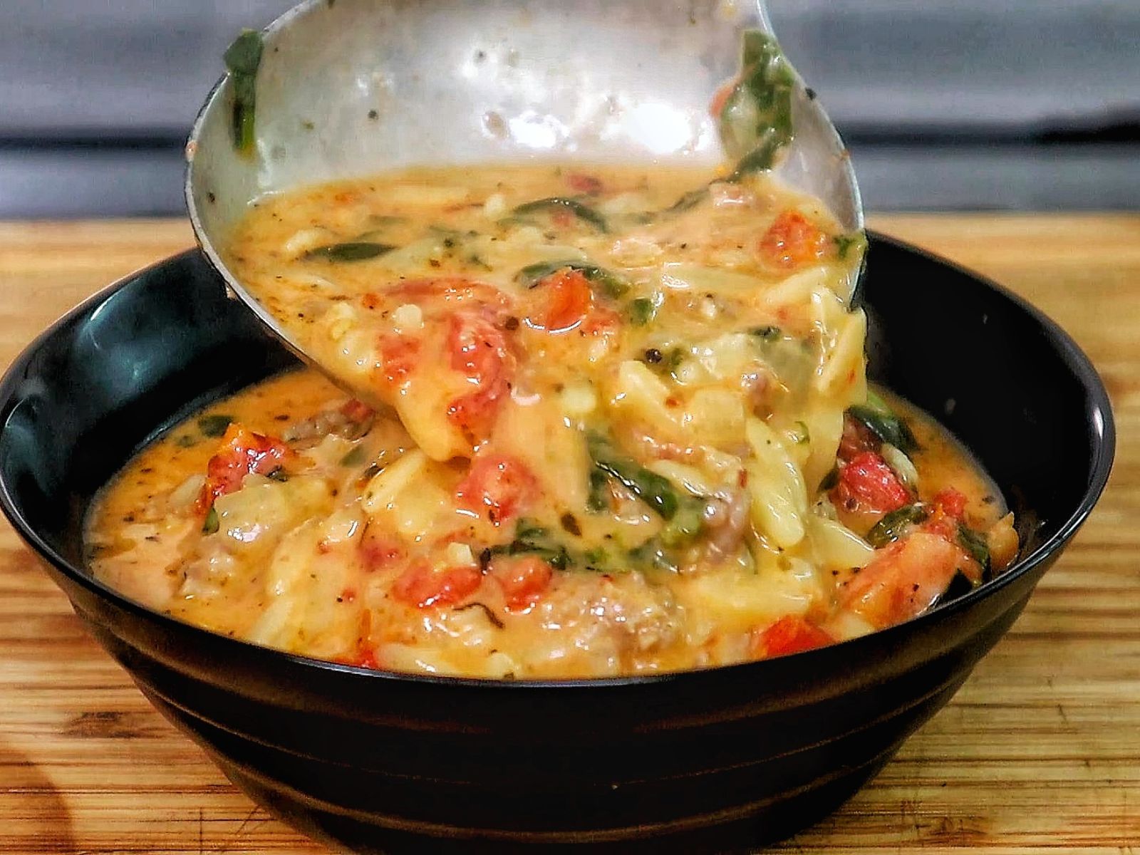 A creamy bowl of sausage orzo soup filled with tomatoes, spinach, and tender pasta, topped with fresh basil and melted Parmesan.