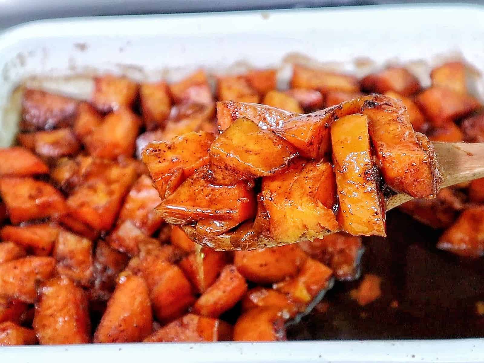 Southern candied yams featuring tender sweet potato chunks coated in a glossy brown sugar syrup with flecks of cinnamon and spices.