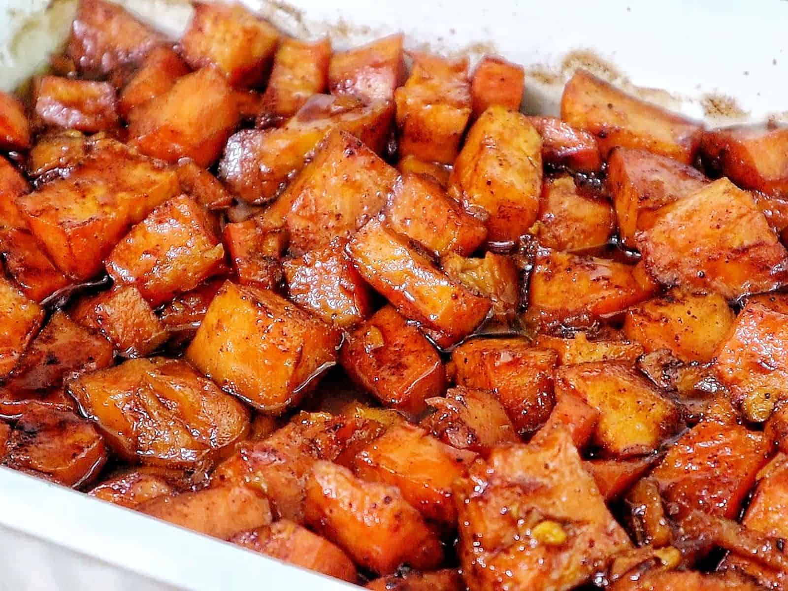 Southern candied yams featuring tender sweet potato chunks coated in a glossy brown sugar syrup with flecks of cinnamon and spices.