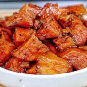 Southern candied yams featuring tender sweet potato chunks coated in a glossy brown sugar syrup with flecks of cinnamon and spices.