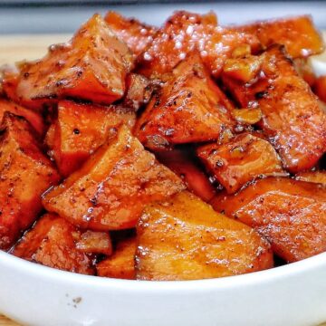 Southern candied yams featuring tender sweet potato chunks coated in a glossy brown sugar syrup with flecks of cinnamon and spices.