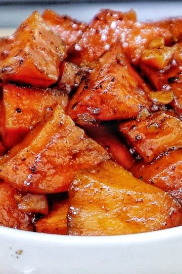 Southern candied yams featuring tender sweet potato chunks coated in a glossy brown sugar syrup with flecks of cinnamon and spices.