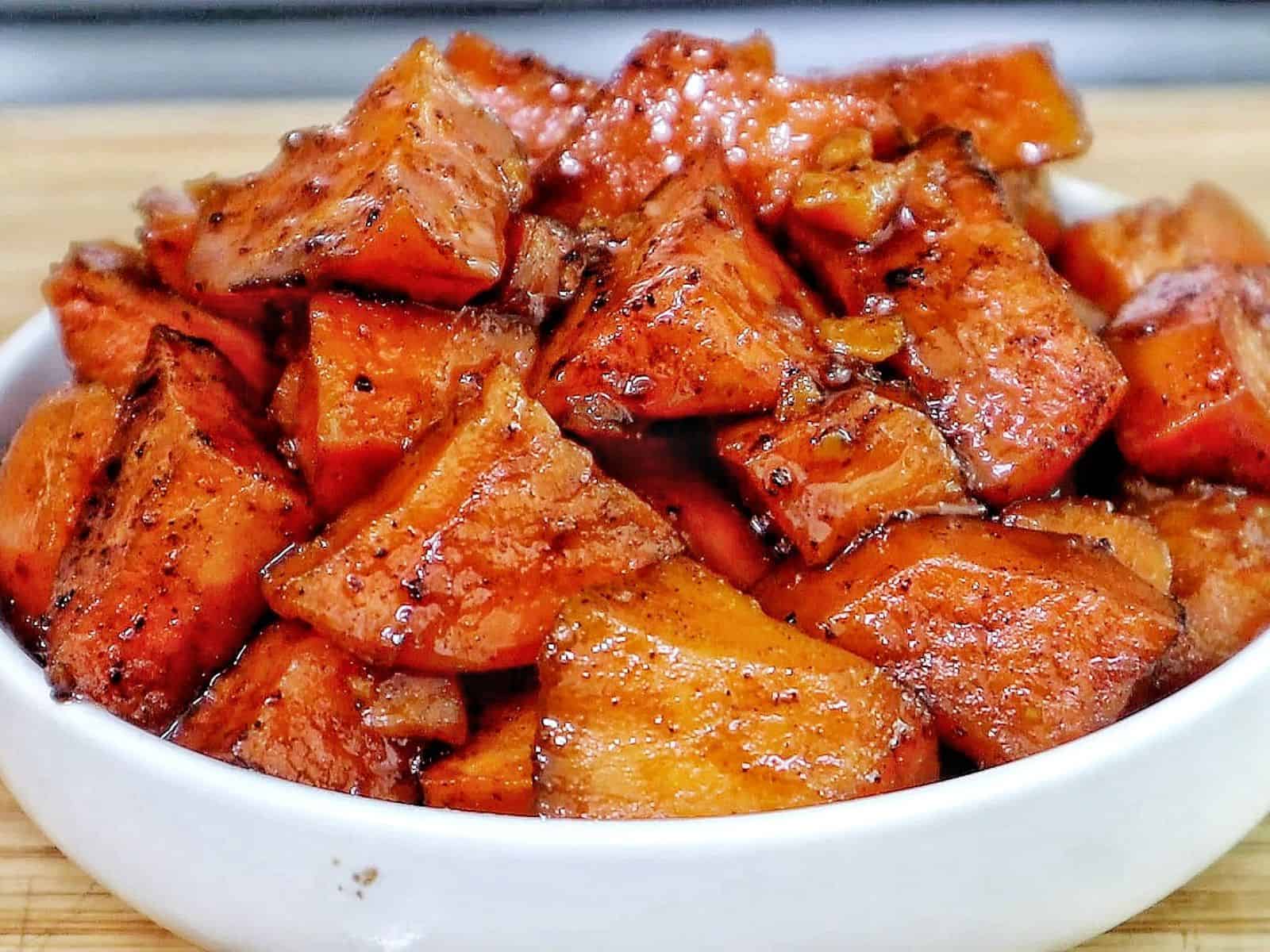 Southern candied yams featuring tender sweet potato chunks coated in a glossy brown sugar syrup with flecks of cinnamon and spices.