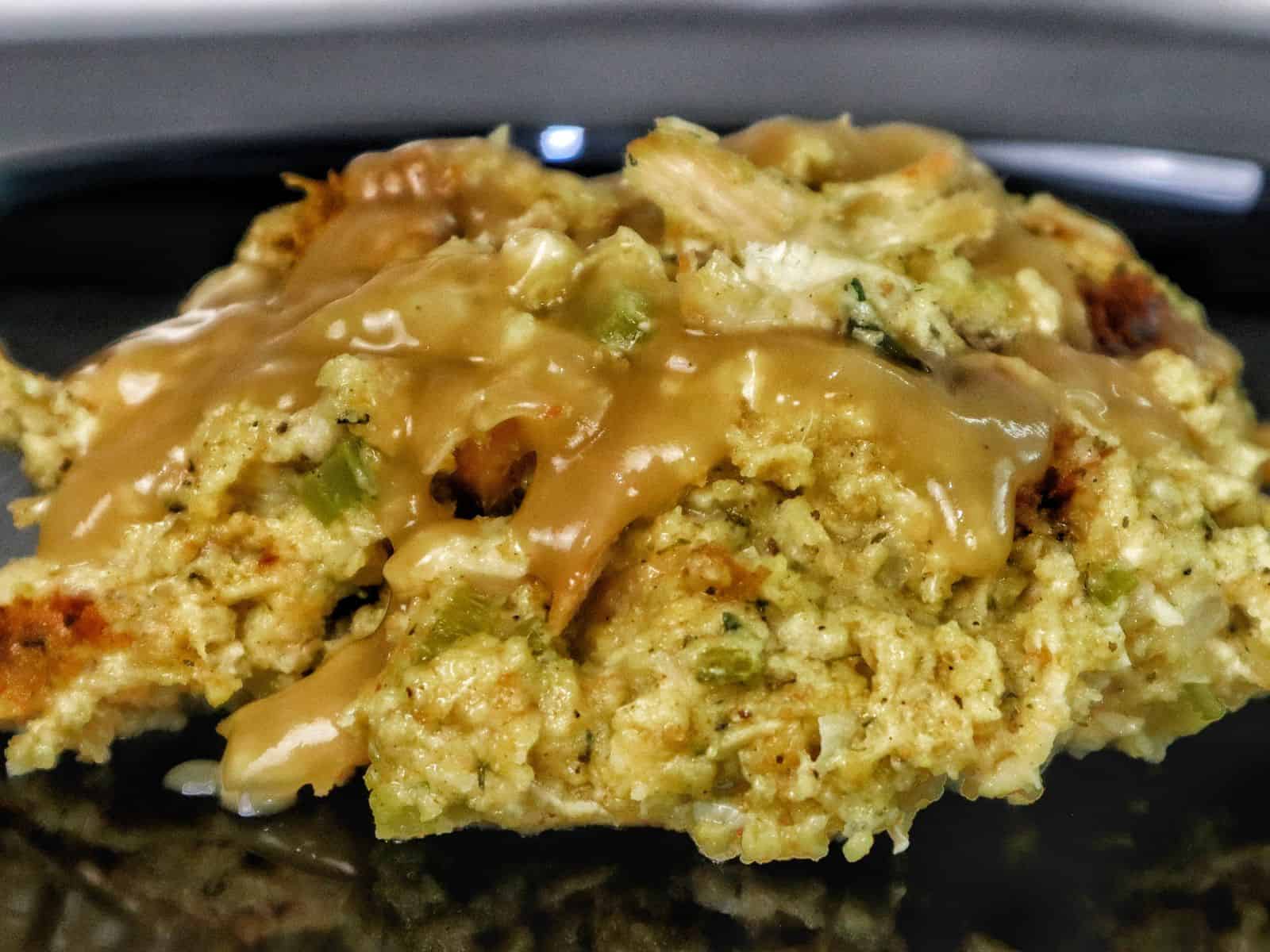Golden Southern cornbread dressing topped with rich brown gravy, showing tender chunks of shredded chicken and herbs.
