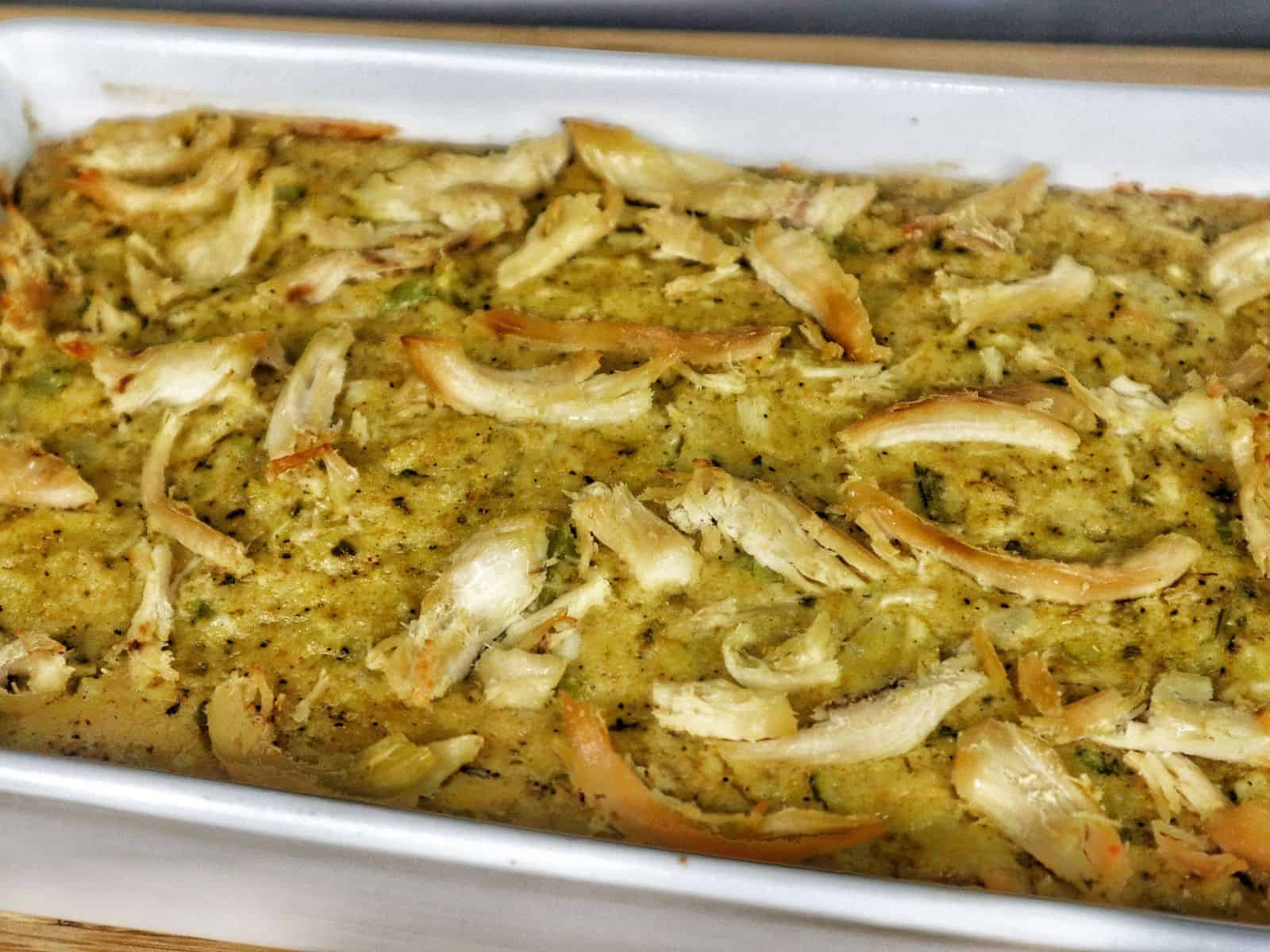 Golden Southern cornbread dressing topped with rich brown gravy, showing tender chunks of shredded chicken and herbs.