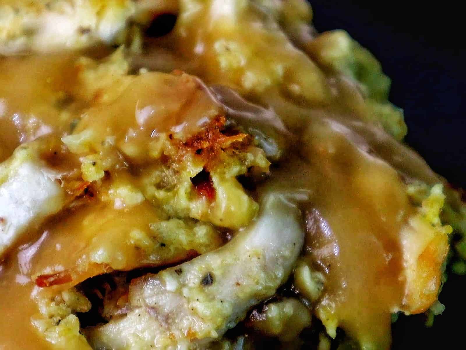 Golden Southern cornbread dressing topped with rich brown gravy, showing tender chunks of shredded chicken and herbs.