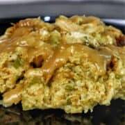 Golden Southern cornbread dressing topped with rich brown gravy, showing tender chunks of shredded chicken and herbs.
