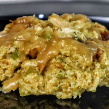 Golden Southern cornbread dressing topped with rich brown gravy, showing tender chunks of shredded chicken and herbs.