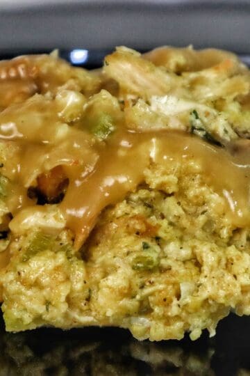 Golden Southern cornbread dressing topped with rich brown gravy, showing tender chunks of shredded chicken and herbs.
