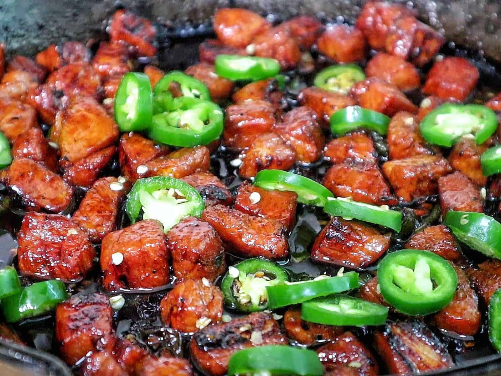 A plate of glazed pork cubes coated in a dark, sticky sweet sauce, topped with sliced fresh jalapeños.