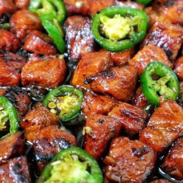 A plate of glazed pork cubes coated in a dark, sticky sweet sauce, topped with sliced fresh jalapeños.