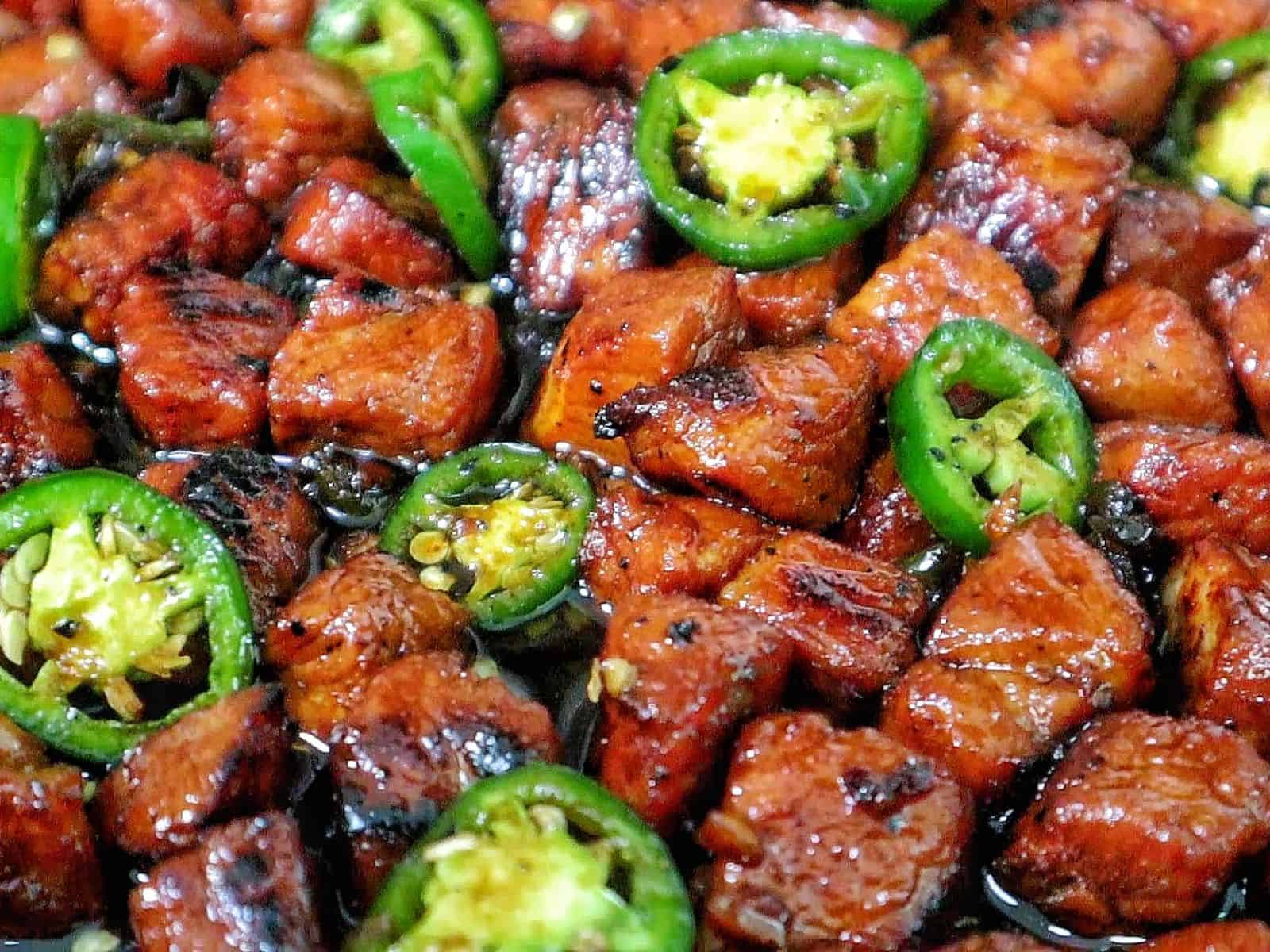 A plate of glazed pork cubes coated in a dark, sticky sweet sauce, topped with sliced fresh jalapeños.