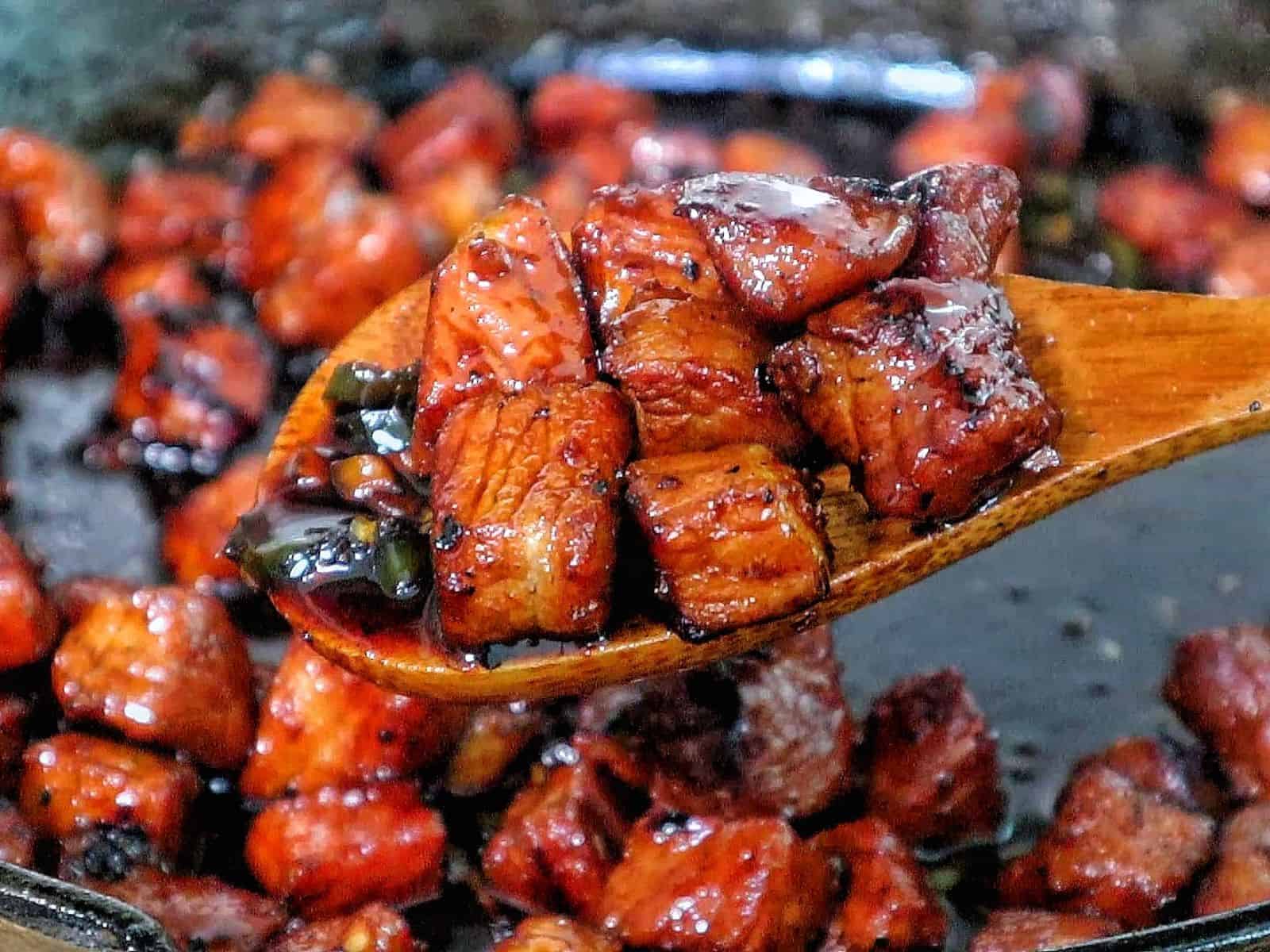 A plate of glazed pork cubes coated in a dark, sticky sweet sauce, topped with sliced fresh jalapeños.