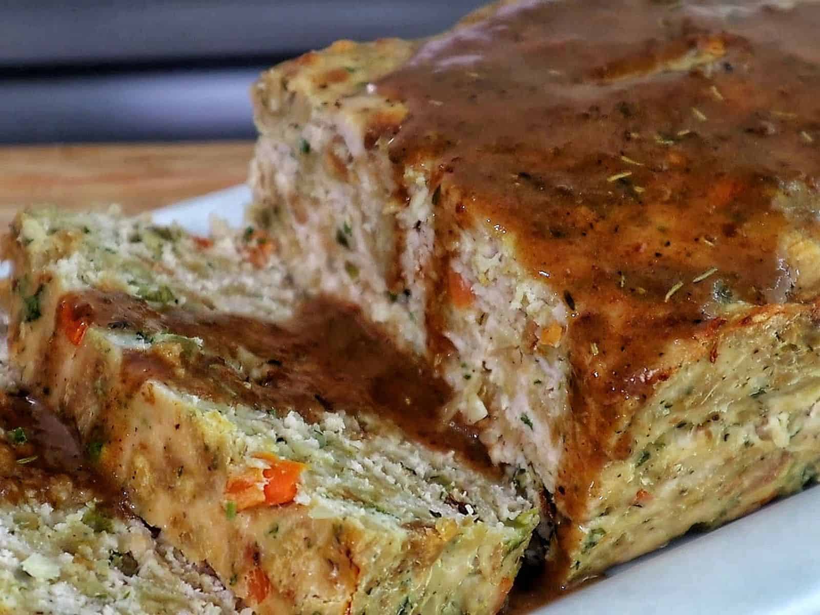 Turkey stuffing meatloaf sliced on a white plate topped with brown gravy.