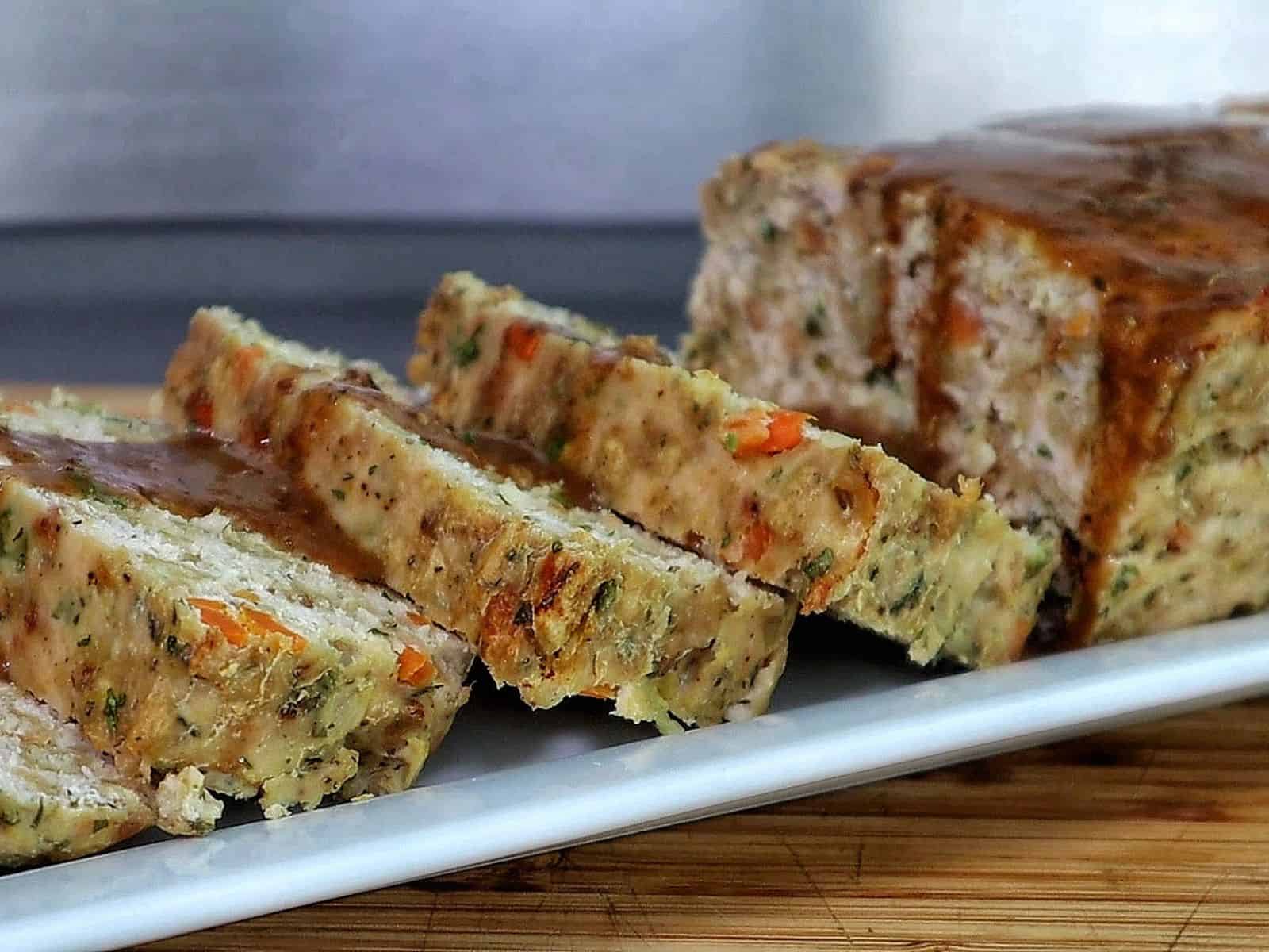 Turkey stuffing meatloaf sliced on a white plate topped with brown gravy.