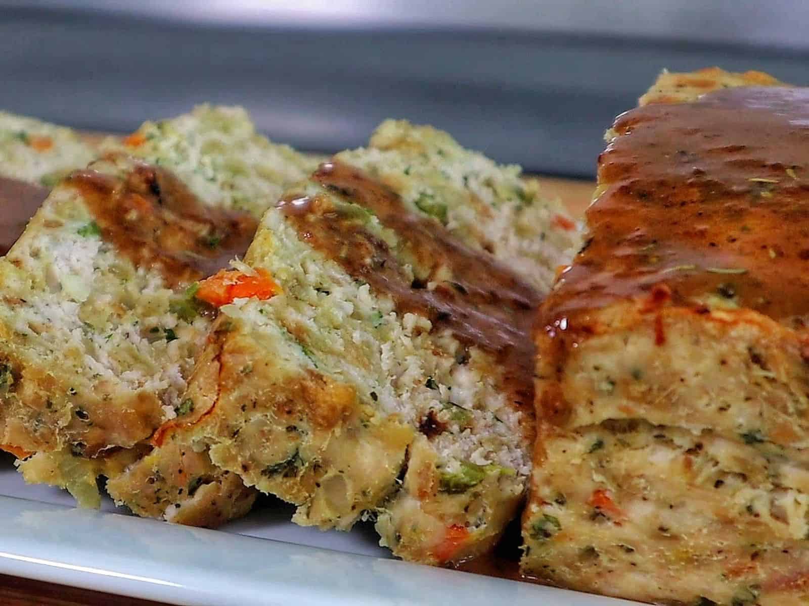 Turkey stuffing meatloaf sliced on a white plate topped with brown gravy.