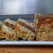 Turkey stuffing meatloaf sliced on a white plate topped with brown gravy.