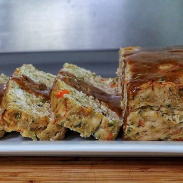 Turkey stuffing meatloaf sliced on a white plate topped with brown gravy.
