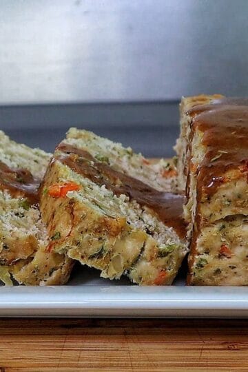 Turkey stuffing meatloaf sliced on a white plate topped with brown gravy.