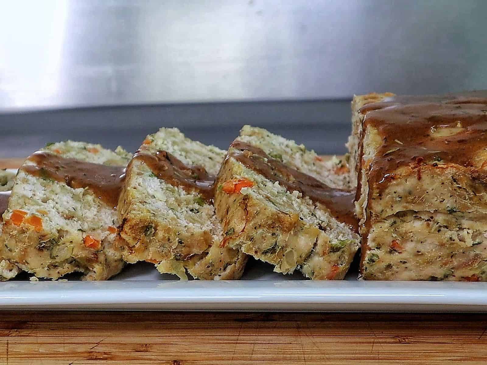 Turkey stuffing meatloaf sliced on a white plate topped with brown gravy.