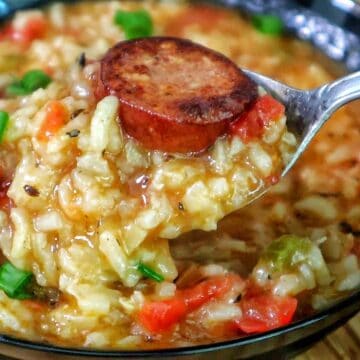 A bowl of jambalaya soup filled with tender rice, sliced smoked sausage, chunks of chicken, tomatoes, and vegetables in a rich, seasoned broth, garnished with chopped green onions