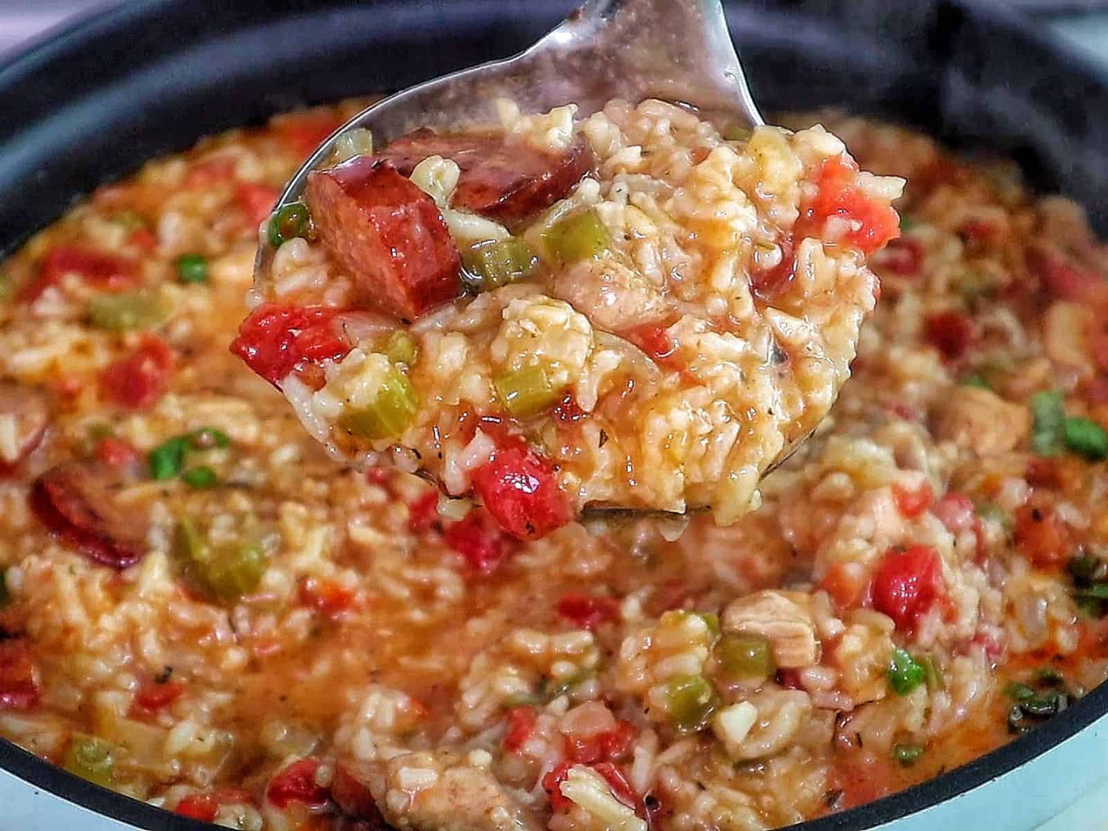 A bowl of jambalaya soup filled with tender rice, sliced smoked sausage, chunks of chicken, tomatoes, and vegetables in a rich, seasoned broth, garnished with chopped green onions.