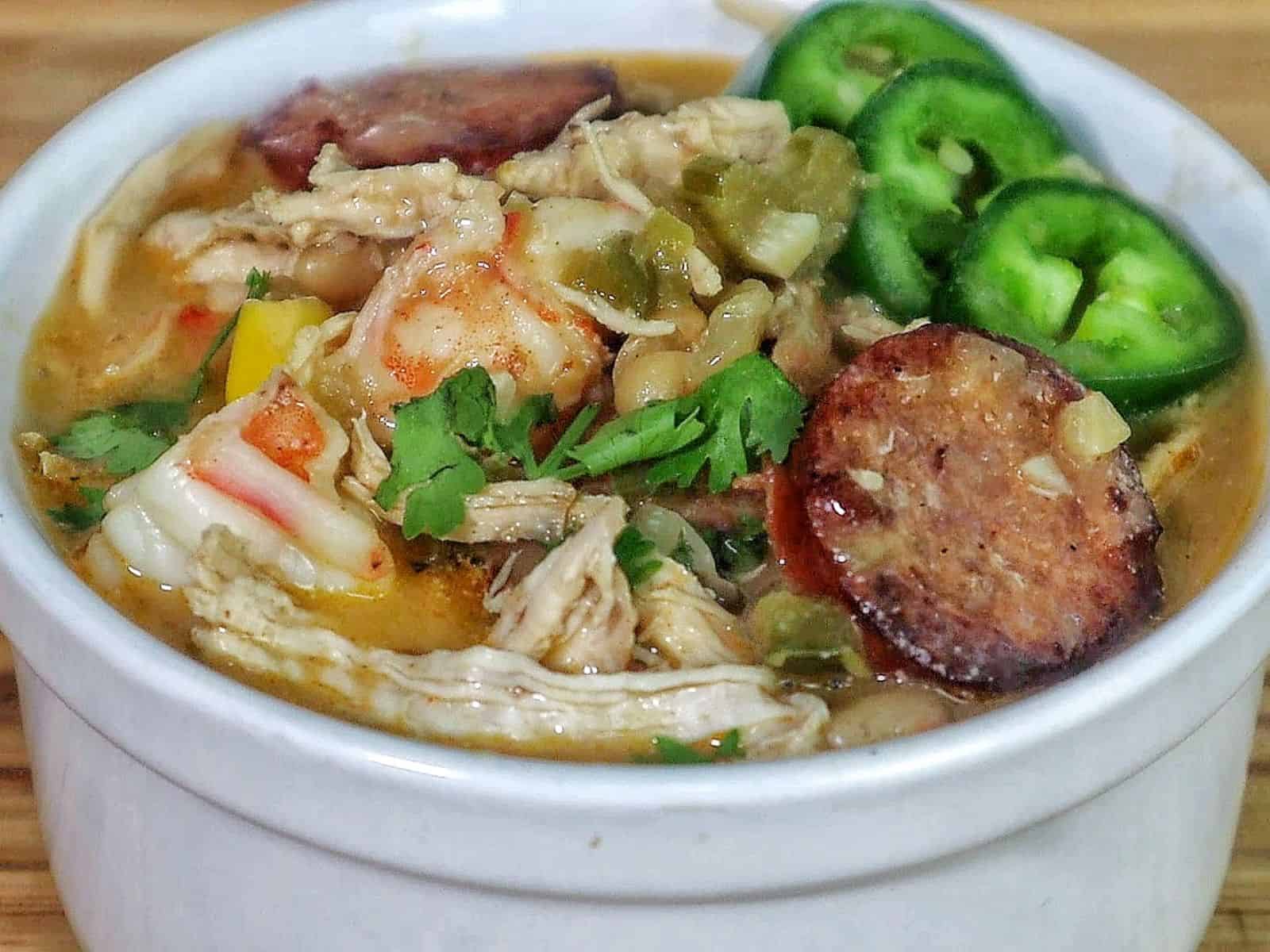 Bowl of Cajun white chicken chili filled with shredded chicken, shrimp, sliced sausage, white beans, corn, and peppers, topped with fresh cilantro and sliced jalapenos.