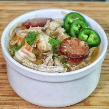 Bowl of Cajun white chicken chili filled with shredded chicken, shrimp, sliced sausage, white beans, corn, and peppers, topped with fresh cilantro and sliced jalapenos.