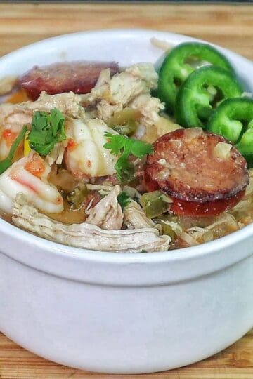 Bowl of Cajun white chicken chili filled with shredded chicken, shrimp, sliced sausage, white beans, corn, and peppers, topped with fresh cilantro and sliced jalapenos.