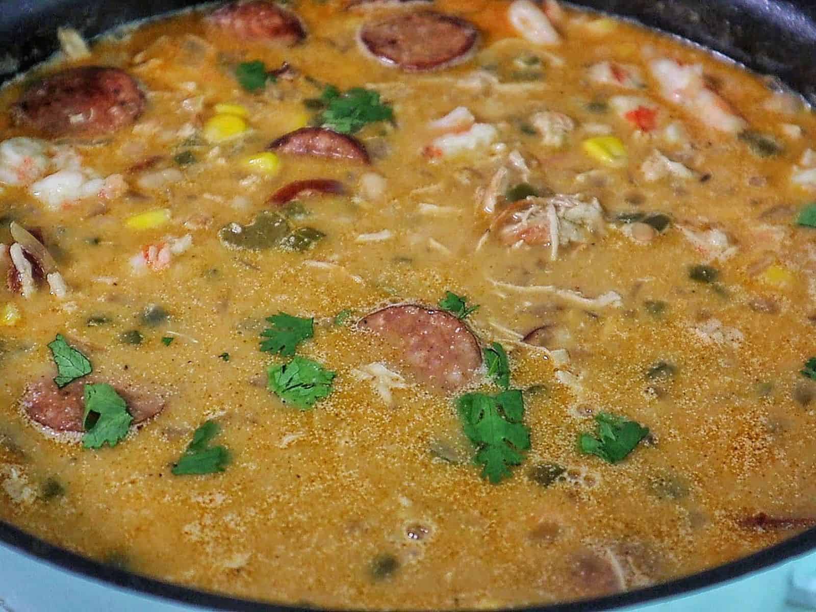Bowl of Cajun white chicken chili filled with shredded chicken, shrimp, sliced sausage, white beans, corn, and peppers, topped with fresh cilantro and sliced jalapenos.