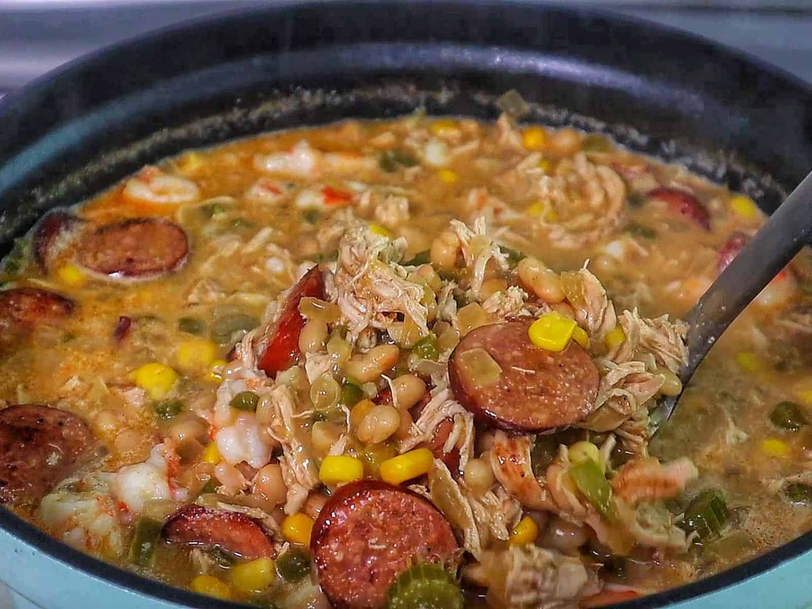 bowl of Cajun white chicken chili filled with shredded chicken, shrimp, sliced sausage, white beans, corn, and peppers, topped with fresh cilantro and sliced jalapenos.