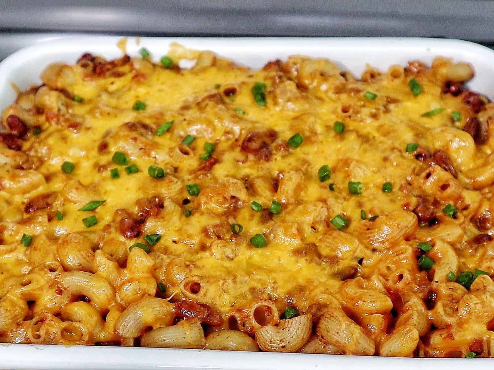 Cheesy chili mac casserole baked until bubbly and golden, made with elbow macaroni, ground beef, kidney beans, and melted cheddar cheese, garnished with green onions.