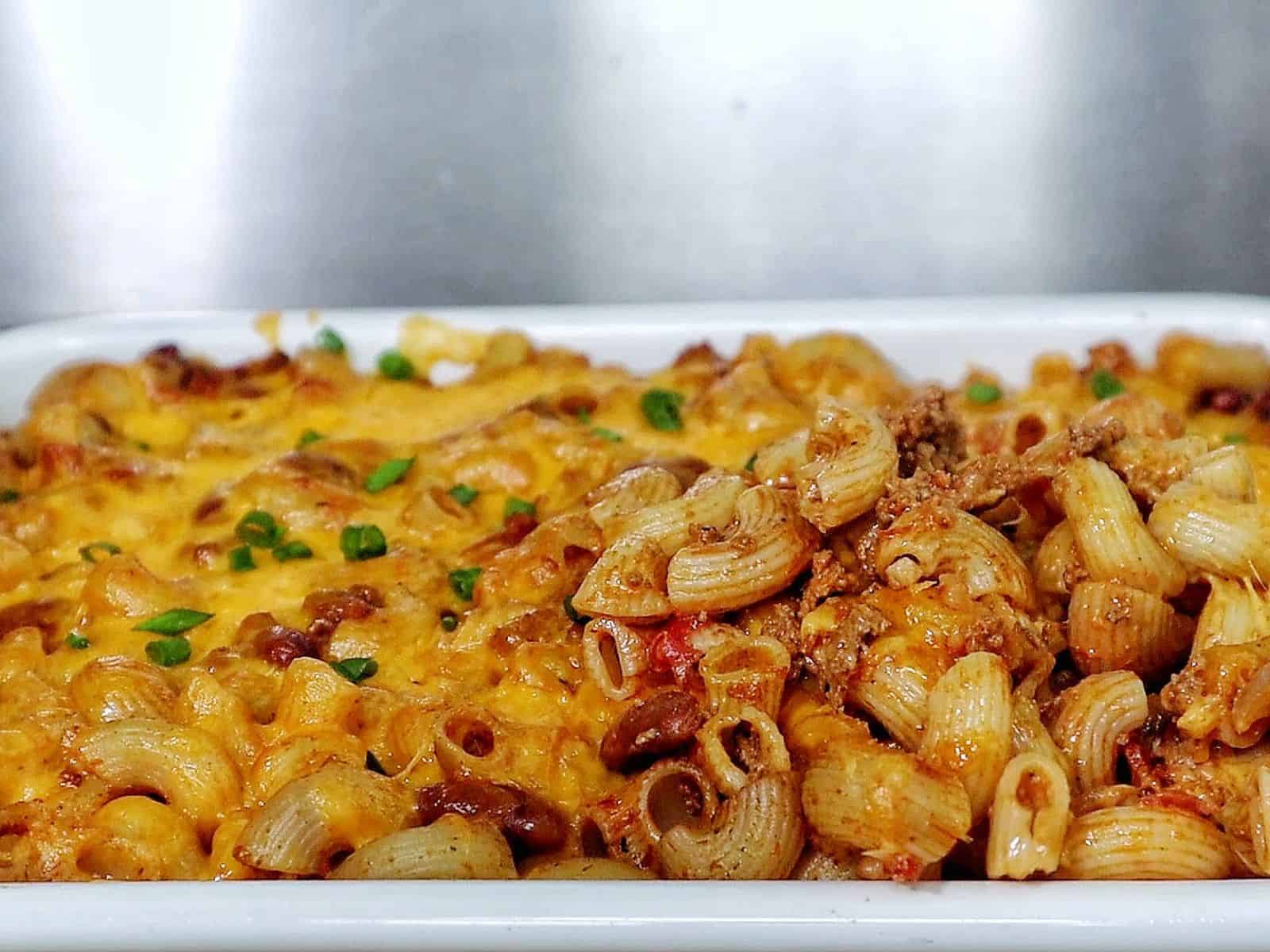 Cheesy chili mac casserole baked until bubbly and golden, made with elbow macaroni, ground beef, kidney beans, and melted cheddar cheese, garnished with green onions.