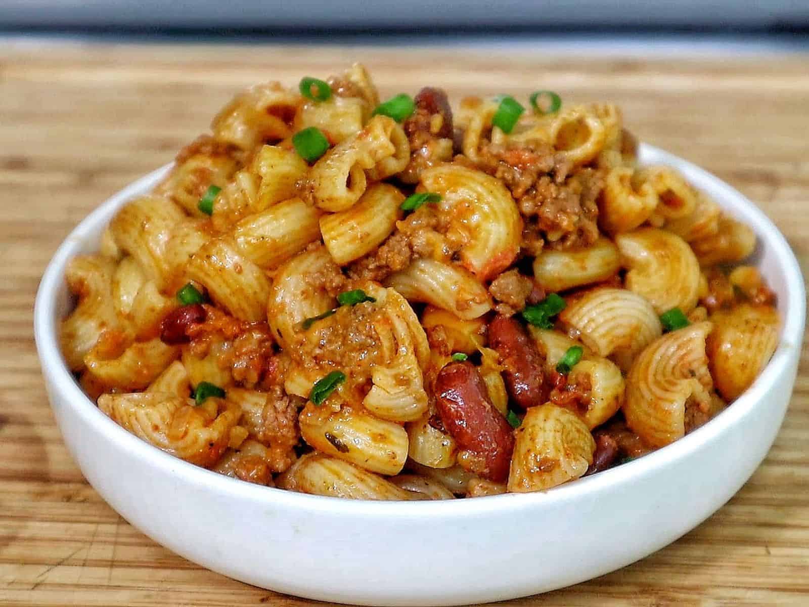 Cheesy chili mac casserole baked until bubbly and golden, made with elbow macaroni, ground beef, kidney beans, and melted cheddar cheese, garnished with green onions.