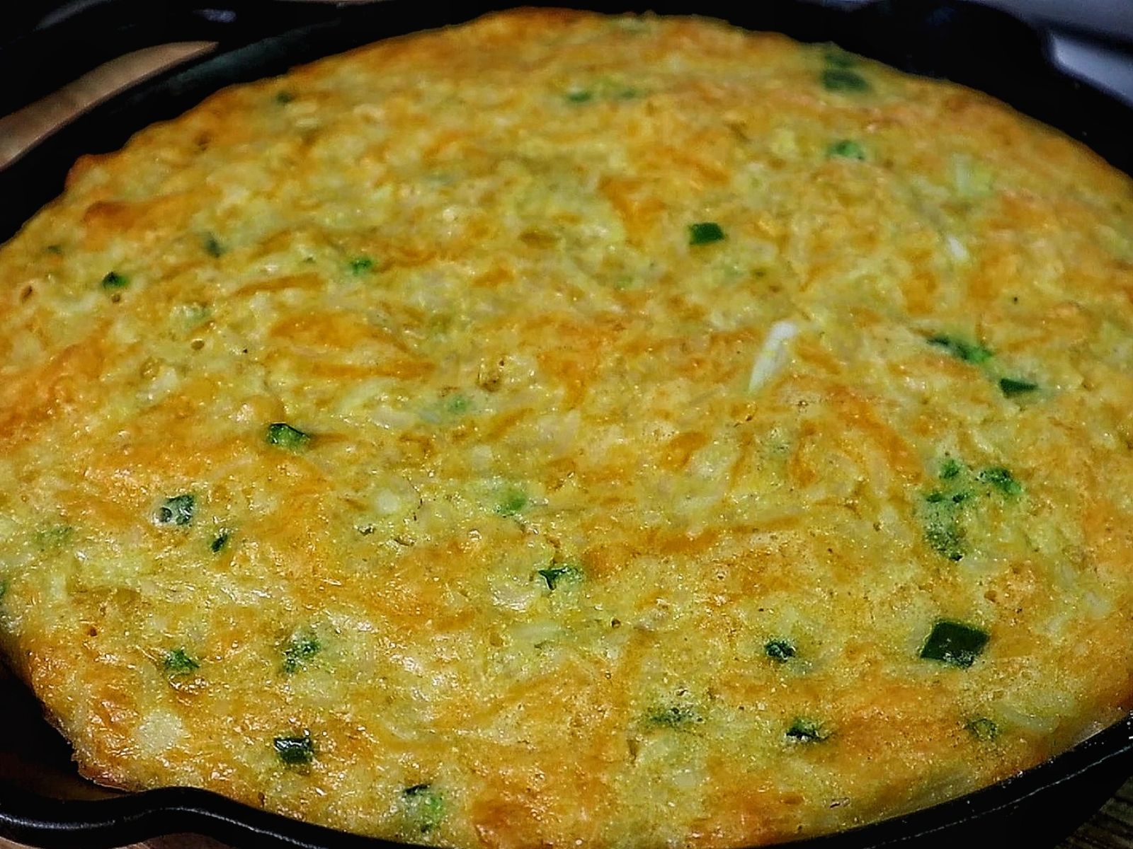 Slice of Creole cornbread made with rice, cheddar cheese, jalapeños, and onions, baked golden brown in a cast iron skillet