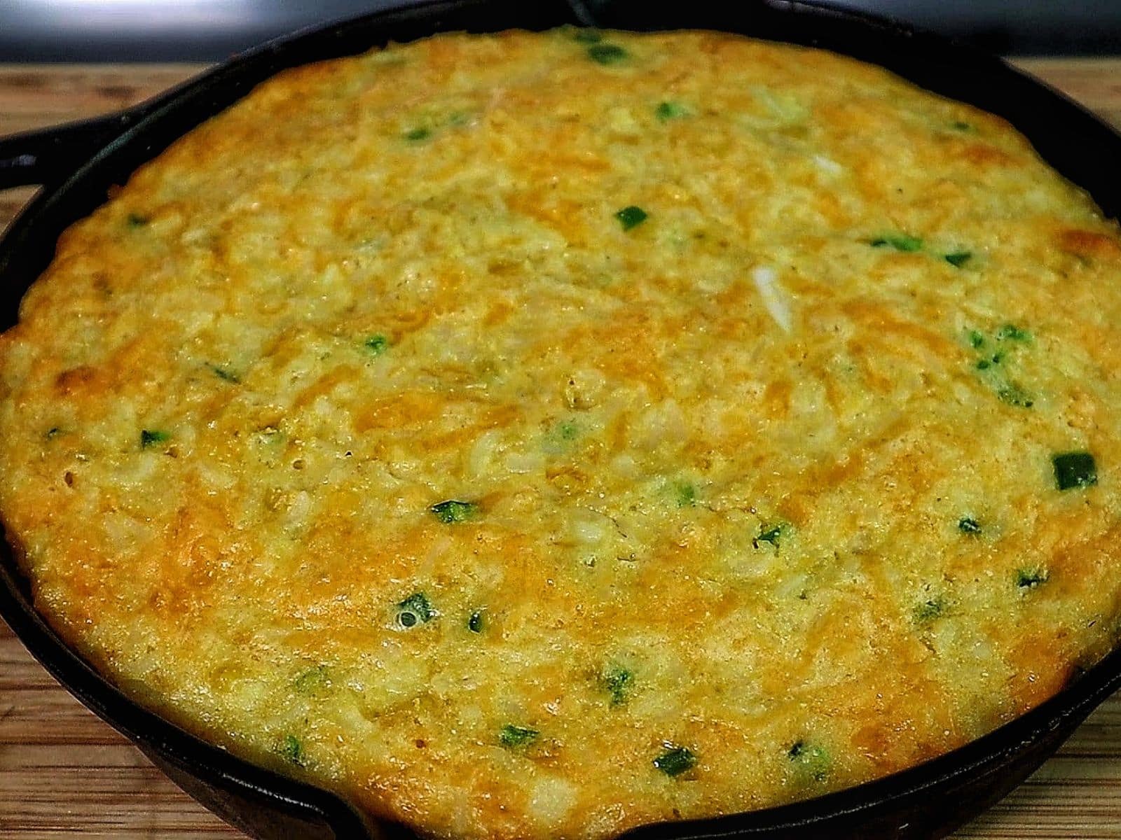 Slice of Creole cornbread made with rice, cheddar cheese, jalapeños, and onions, baked golden brown in a cast iron skillet