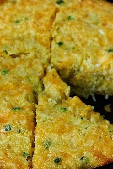 Slice of Creole cornbread made with rice, cheddar cheese, jalapeños, and onions, baked golden brown in a cast iron skillet.