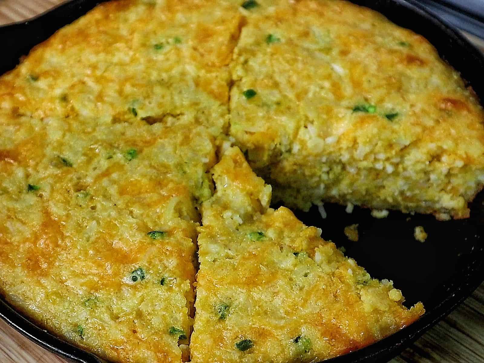 Slice of Creole cornbread made with rice, cheddar cheese, jalapeños, and onions, baked golden brown in a cast iron skillet