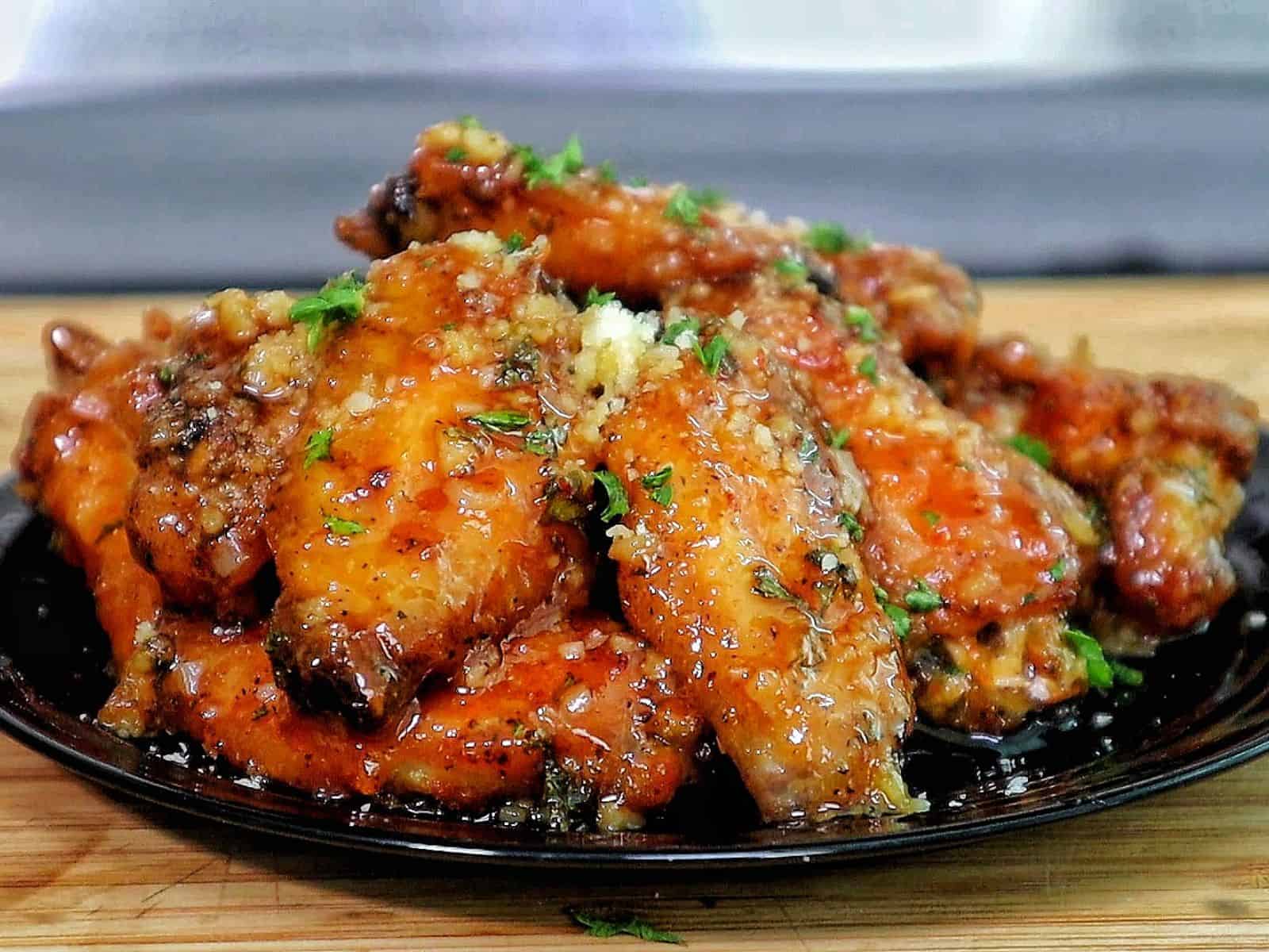 Crispy chicken wings coated in a hot honey garlic Parmesan sauce, garnished with chopped parsley.