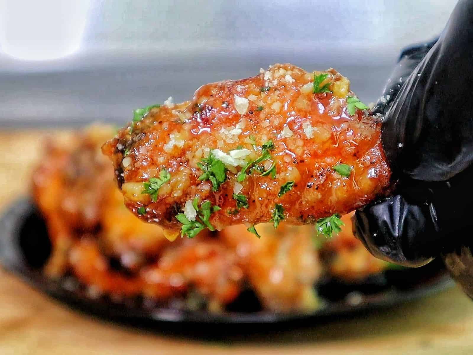 Crispy chicken wings coated in a hot honey garlic Parmesan sauce, garnished with chopped parsley.