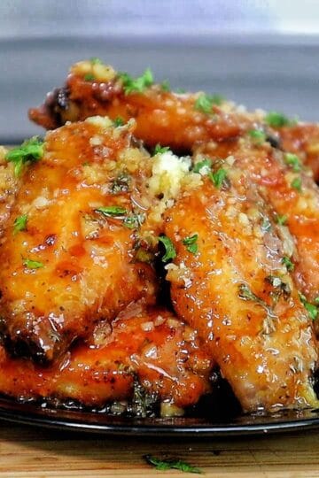 Crispy chicken wings coated in a hot honey garlic Parmesan sauce, garnished with chopped parsley.