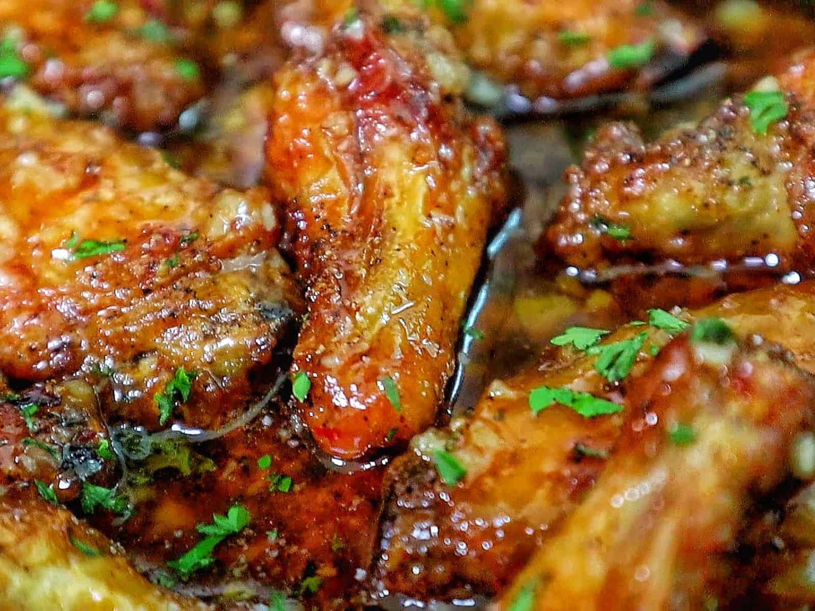 Crispy chicken wings coated in a hot honey garlic Parmesan sauce, garnished with chopped parsley.