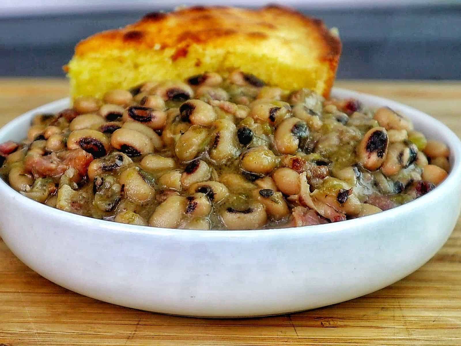 Southern black eyed peas cooked with smoked meat, bacon, and vegetables, served with a golden slice of cornbread resting on top.