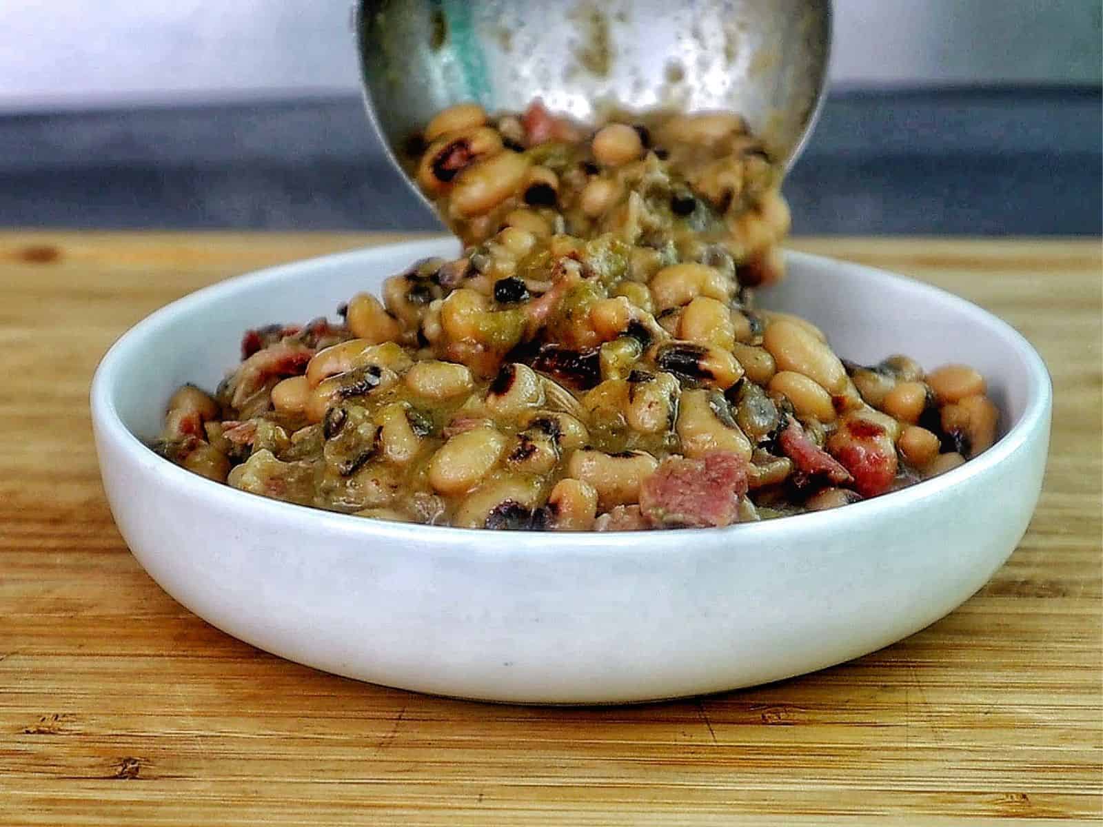 Southern black eyed peas cooked with smoked meat, bacon, and vegetables, served with a golden slice of cornbread resting on top.