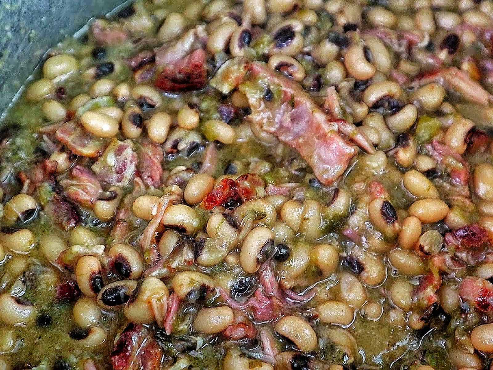 Southern black eyed peas cooked with smoked meat, bacon, and vegetables, served with a golden slice of cornbread resting on top.