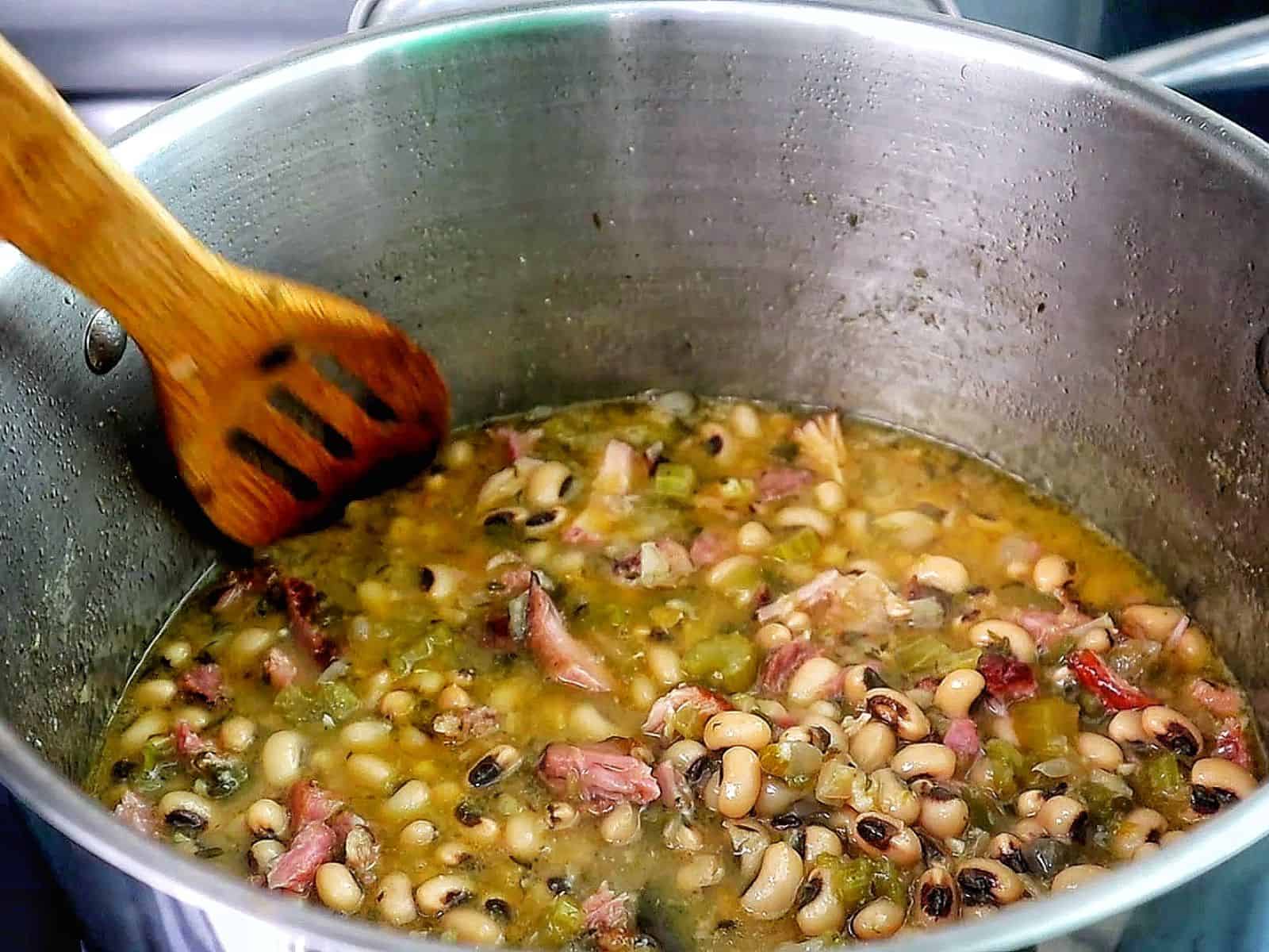 Southern black eyed peas cooked with smoked meat, bacon, and vegetables, served with a golden slice of cornbread resting on top.