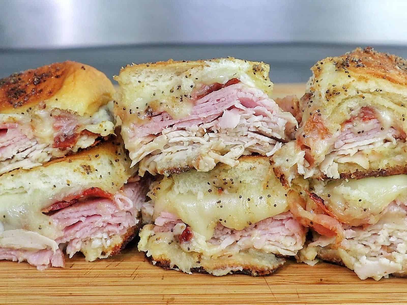 Golden baked Hawaiian roll sliders layered with turkey, ham, crispy bacon, and melted provolone, brushed with garlic butter.